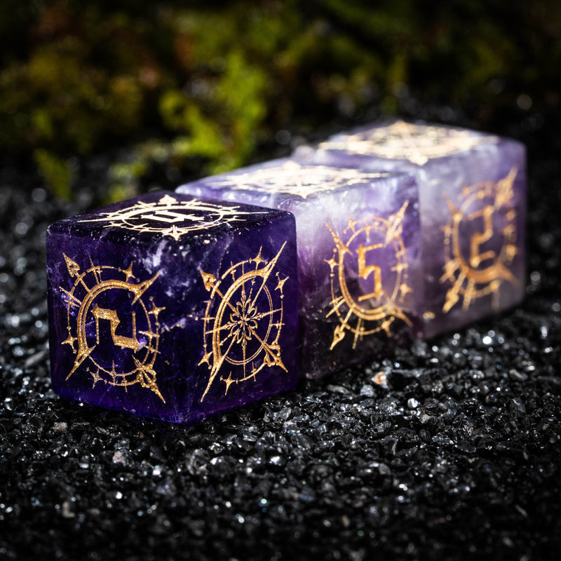 two purple dices with gold designs on them